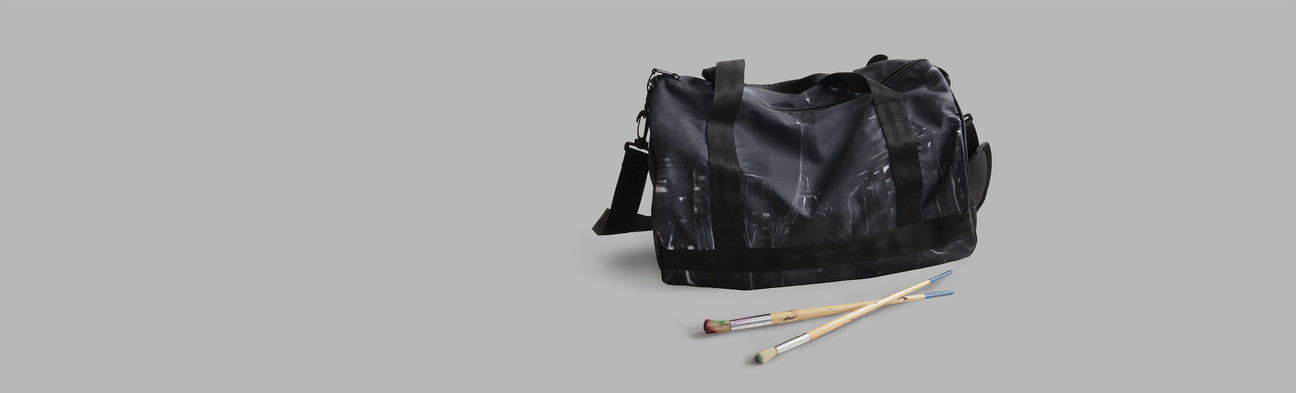 Black duffel bag with paintbrushes on a gray background